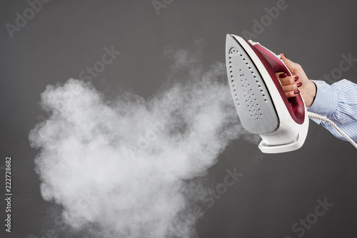 Fototapet Woman holds an iron with steam on gray background