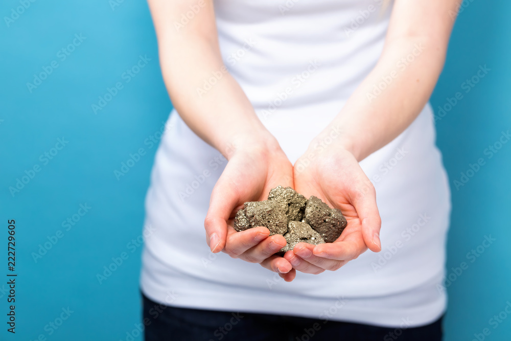 Young woman holding raw gold nuggets on a blue background Young woman holding raw gold nuggets on a blue background