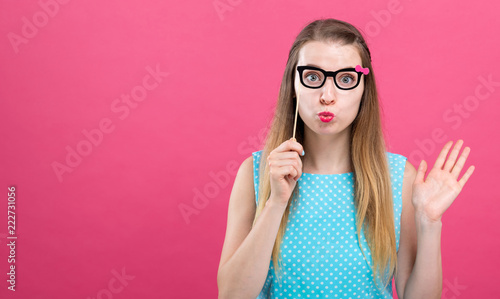Young woman holding a paper glasses party stick on a pink background