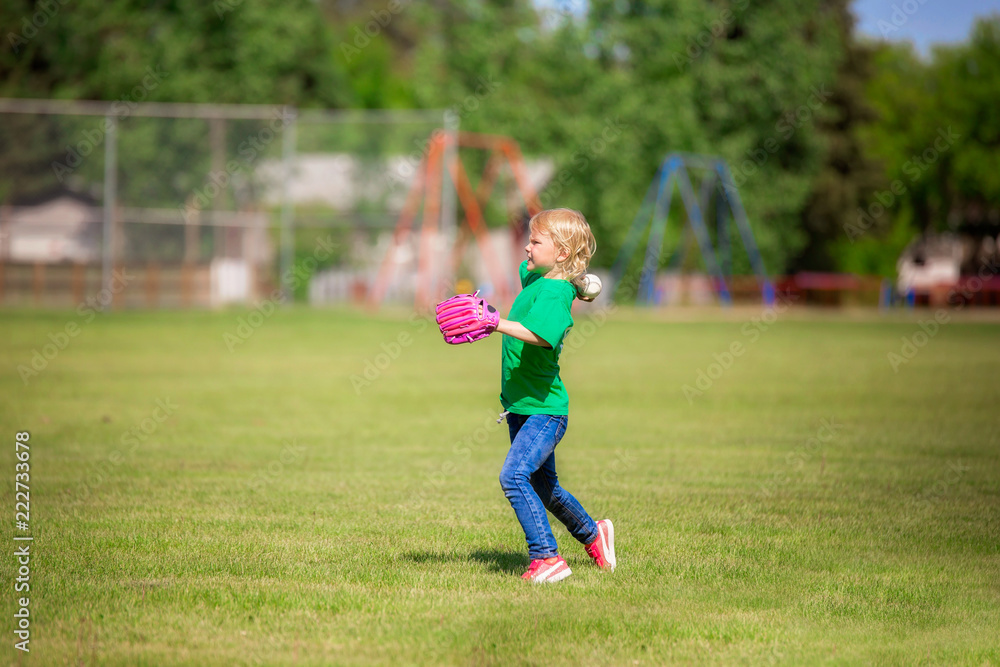 A six year old girl in jeans and t-shirt in action throwing a baseball on green grass on a summer afternoon A six year old girl in jeans and t-shirt in action throwing a baseball on green grass on a summer afternoon