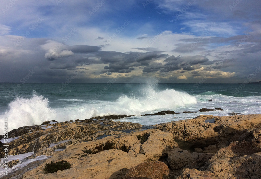 Waves crowned with foam runing towards rocks on the shore with a dramatic sky in background