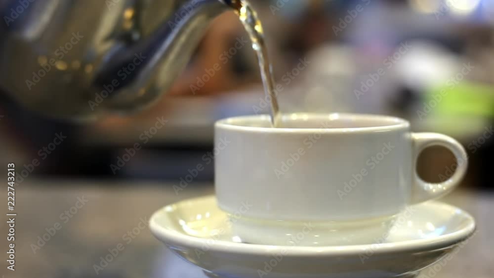 Soft focused pouring steaming hot tea from teapot into a ceramic cup in a restaurant. Soft focused pouring steaming hot tea from teapot into a ceramic cup in a restaurant.