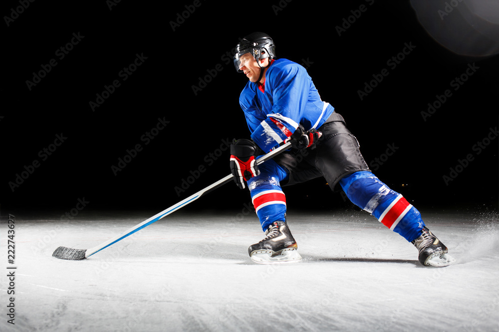 Fototapeta premium Hockey player with stick turning around skating on ice against black background