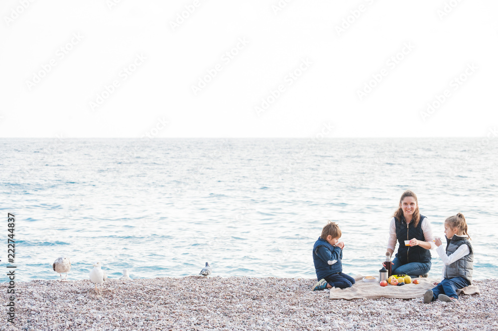 happy family consisting of three person on sea shore picnic in cold weather happy family consisting of three person on sea shore picnic in cold weather