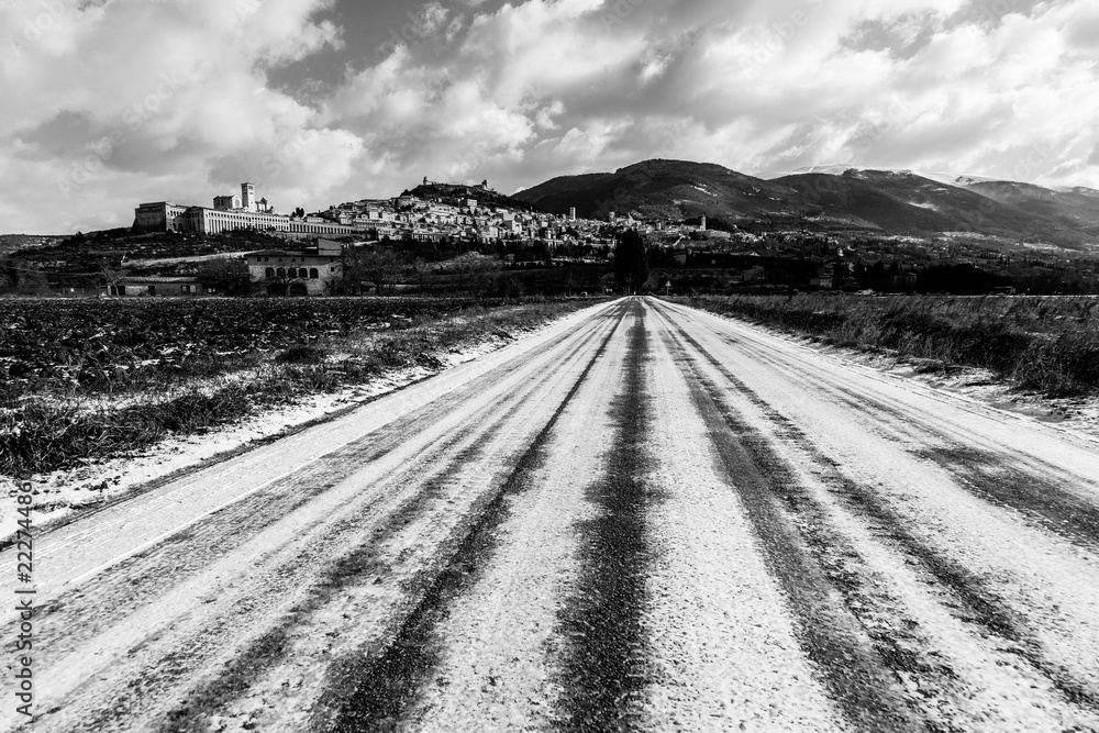 View of Assisi town (Umbria) in winter, with a field covered by snow and sky with white clouds View of Assisi town (Umbria) in winter, with a field covered by snow and sky with white clouds