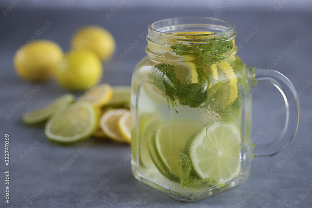 Refreshing lemonade with lemon and lime slices and mint leaves in a glass mug on a gray background. Refreshing lemonade with lemon and lime slices and mint leaves in a glass mug on a gray background.