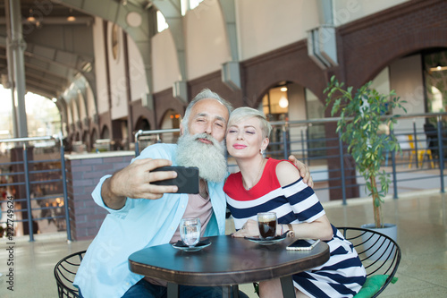 Senior couple makes a selfie using a phone in the cafe. Celebrating anniversary.