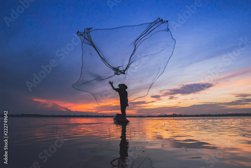 Asian fisherman on wooden boat casting a net for catching freshwater fish in nature