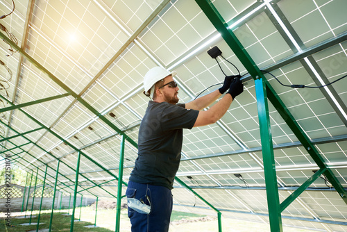 Professional worker installing solar panels on the green metal construction, using different equipment, wearing helmet. Innovative solution for energy solving. Use renewable resources. Green energy.