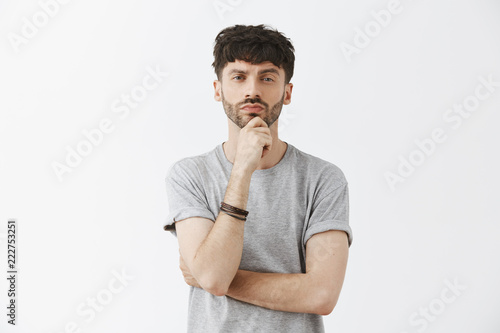 Waist-up shot of good-looking thoughtful male genius with dark hair and beard holdin hand on chin and pursing lips looking seriously at camera having plan or considering how make things right