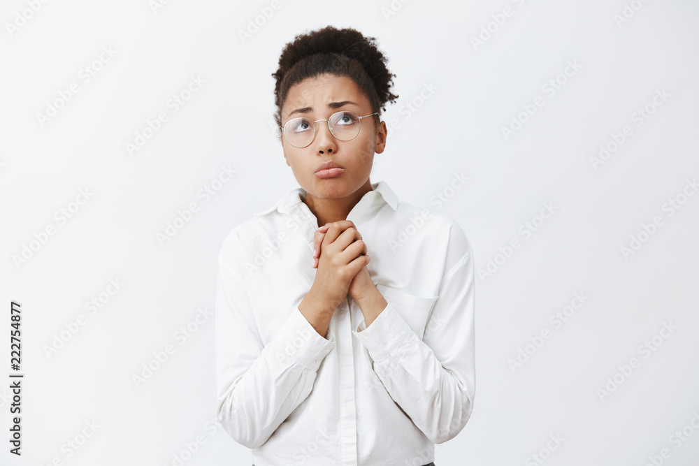 Upset timid and insecure good-looking african-american girl in glasses and white collar shirt, clenching palms and frowning, gazing up with sadness and miserable expression over gray background Upset timid and insecure good-looking african-american girl in glasses and white collar shirt, clenching palms and frowning, gazing up with sadness and miserable expression over gray background