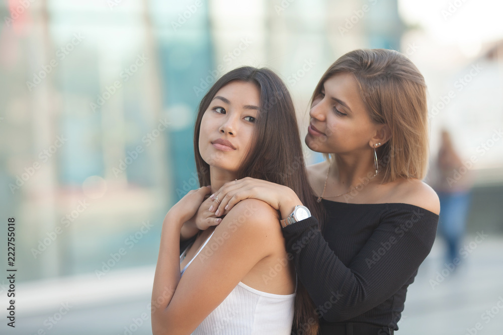 Two young women hugging outdoors. Asian girl looking at the camera and smiling. Best friends Two young women hugging outdoors. Asian girl looking at the camera and smiling. Best friends