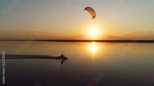 Orange sunset over a lake on which a lonely kitesurfer rushes