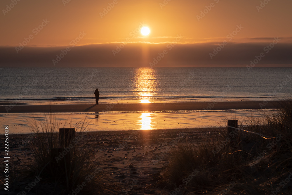 person looking out to sea at low tide with sun reflection