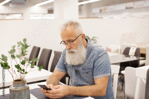 Handsome old man dressed in smart casual style and eyeglasses is using a smartphone while sitting at office.