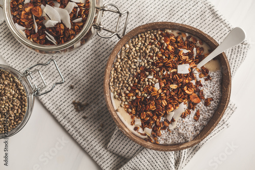 Smoothie bowl with granola, chia pudding and hemp seeds in coconut shell bowl.