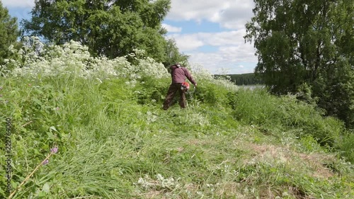 A man farmer mows the tall grass for hay making on a hill photo