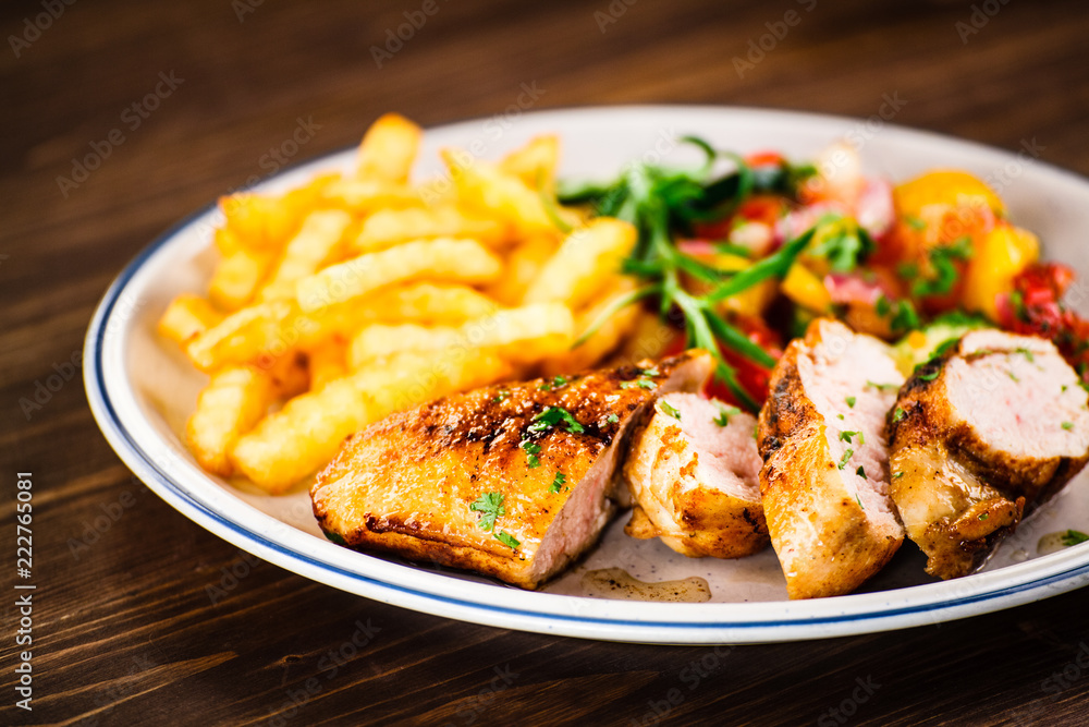 Grilled chicken fillet with french fries on wooden background