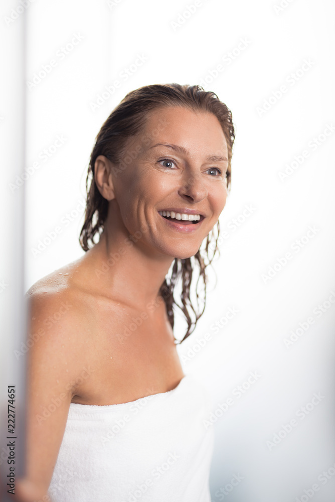 Seeing something pleasant. Portrait of attractive lady with wet hair walking out from bathroom. She is wearing soft towel and looking away with wide smile Seeing something pleasant. Portrait of attractive lady with wet hair walking out from bathroom. She is wearing soft towel and looking away with wide smile