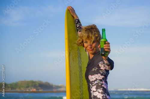 young sexy beautiful and happy surfer woman holding yellow surf board smiling cheerful drinking beer bottle enjoying summer holidays in tropical beach