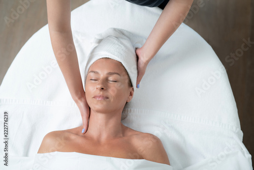 I feel so good. Top view portrait of happy woman with closed eyes lying on massage table during skincare procedure. Masseuse arms touching client neck