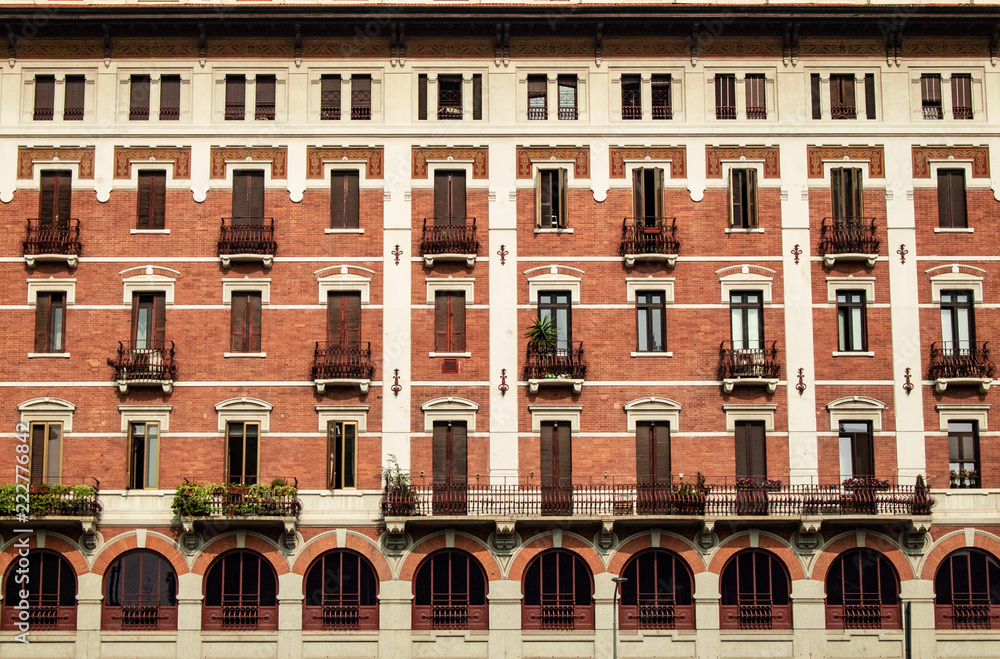 beautiful facade of a Milan building from the early 20th century in red brick with white plaster decorations, Italy