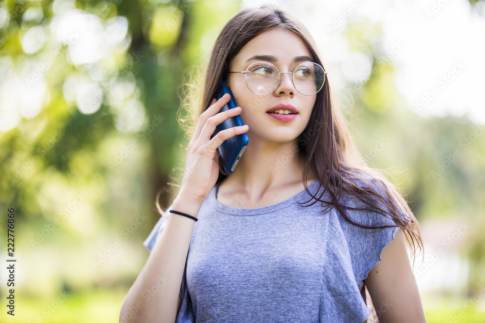 Happy lovely young woman standing and talking on cell phone in park Happy lovely young woman standing and talking on cell phone in park