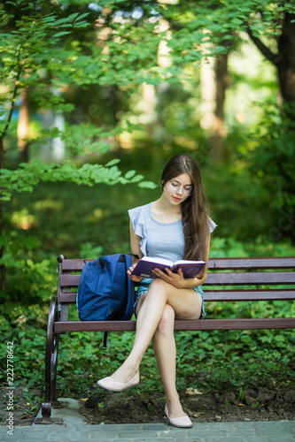 Young woman with a notebook in hands sitting on a park bench