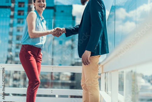 Cheerful girl shaking hand of businessman while speaking with him outside. Happy businesswoman communicating with male concept