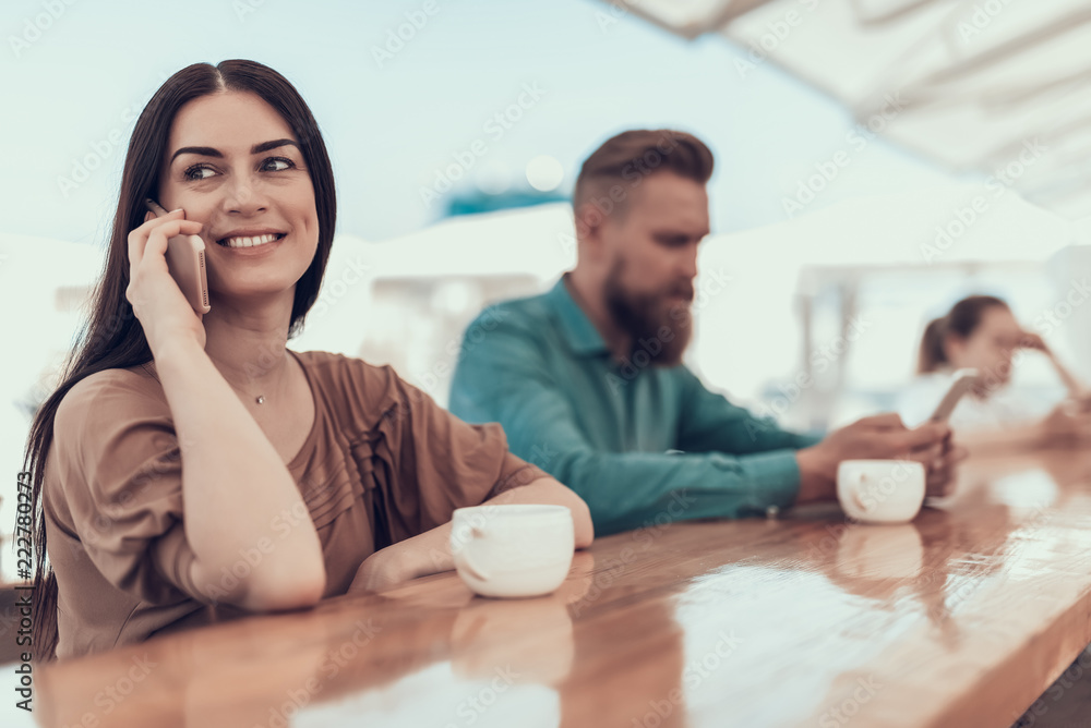 Portrait of cheerful girl telling on mobile while drinking delicious cup of tea. She locating near calm bearded man sending message on gadget Portrait of cheerful girl telling on mobile while drinking delicious cup of tea. She locating near calm bearded man sending message on gadget