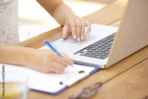 Close-up of woman typing on laptop and writing something