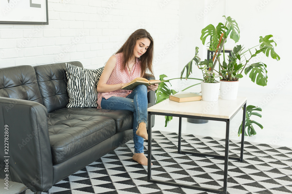 Education and people concept - young woman sitting on the sofa with book Education and people concept - young woman sitting on the sofa with book