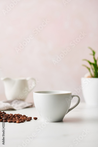 Espresso in a white ceramic coffee cup with roasted coffee beans. Feminine rose background with copy space. Narrow depth of field.