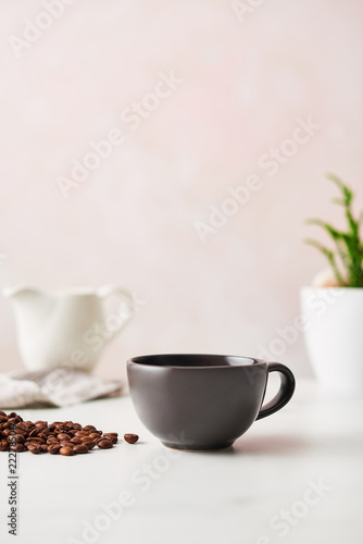 Espresso in a matte black ceramic coffee cup with roasted coffee beans. Feminine rose background with copy space. High resolution image.