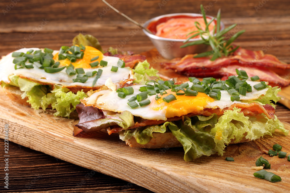 Fried eggs with bacon and chives on wooden background