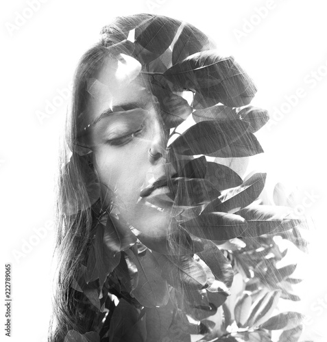 Double exposure portrait of young girl with closed eyes and long wavy hair combined with leaves seemingly growing out of her healthy hair, black and white