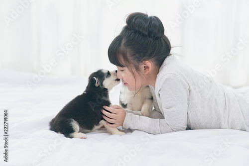 Papier peint Little asian girl lying with  siberian husky puppy on bed