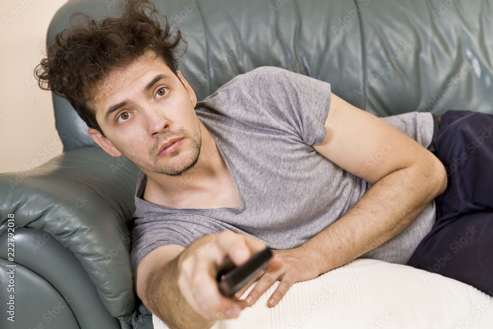 A young man watches television and changes channels while relaxing A young man watches television and changes channels while relaxing