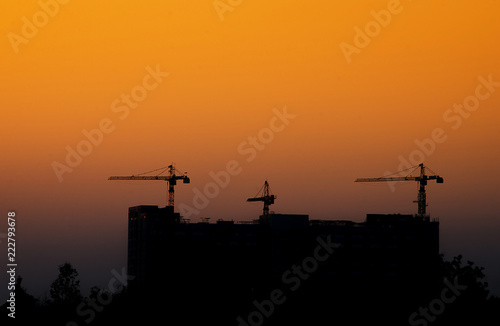 Construction cranes working on the light of the setting sun