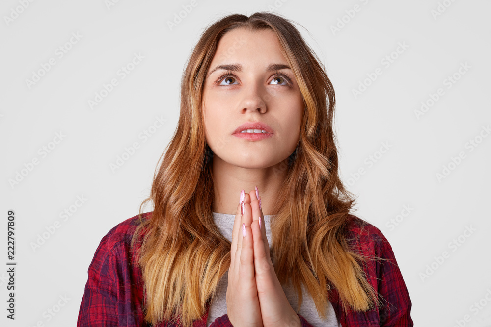 Please, help me! Faithful beautiful woman with serious expression, keeps palms pressed together, looks upwards, believes in good wellness, has pleasant appearance, isolated over white backkground Please, help me! Faithful beautiful woman with serious expression, keeps palms pressed together, looks upwards, believes in good wellness, has pleasant appearance, isolated over white backkground