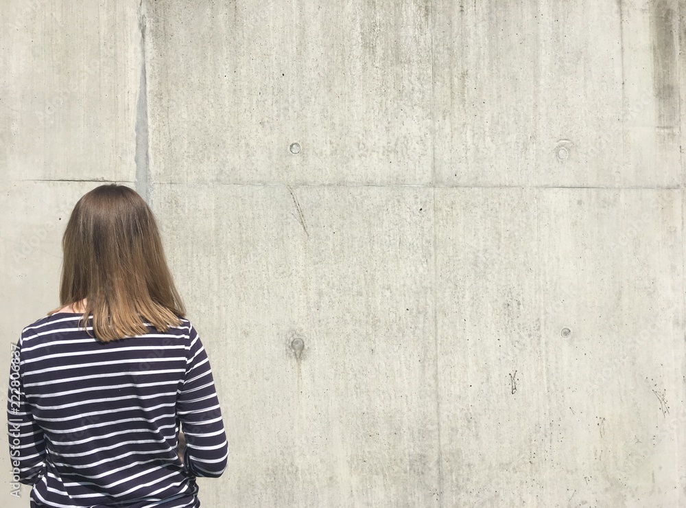 Young woman stood looking at a concrete wall Young woman stood looking at a concrete wall