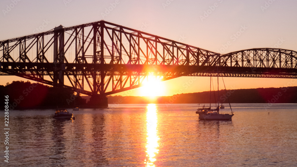 Obraz premium Canada - Bright orange sunset behind the old Quebec City bridge. Bright reflection of the sunlight over the water of a small marina.