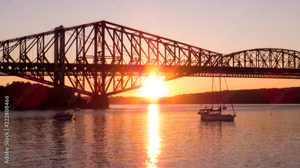 Canada -  Bright orange sunset behind the old Quebec City bridge. Bright reflection of the sunlight over the water of a small marina.