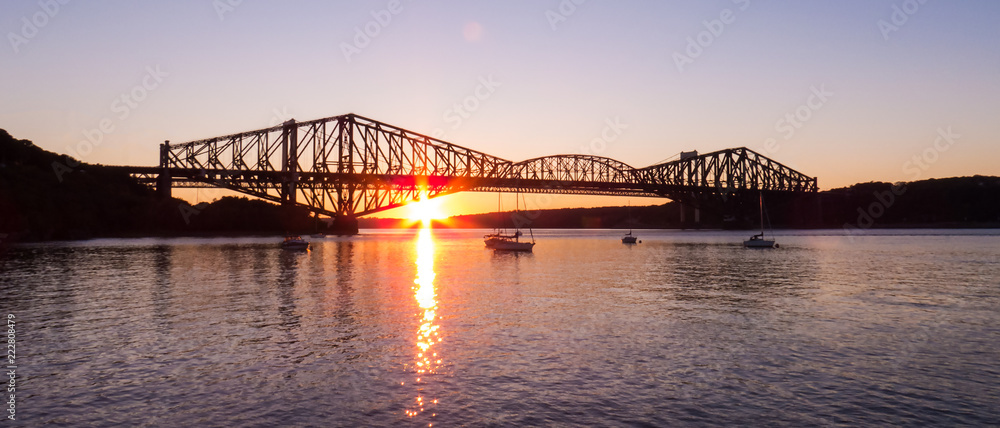 Fototapeta premium Kanada - pionowy zachód słońca za starym mostem Quebec City - odbicie słońca nad wodą małej przystani.