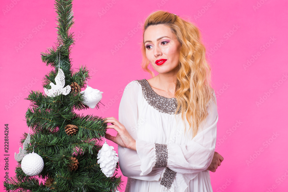 Christmas and people concept - young blonde woman thinking about next year near the christmas tree over the pink background Christmas and people concept - young blonde woman thinking about next year near the christmas tree over the pink background