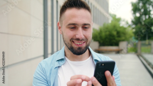 A man with a beard smiling and using a phone in the city street. Medium shot. Soft focus