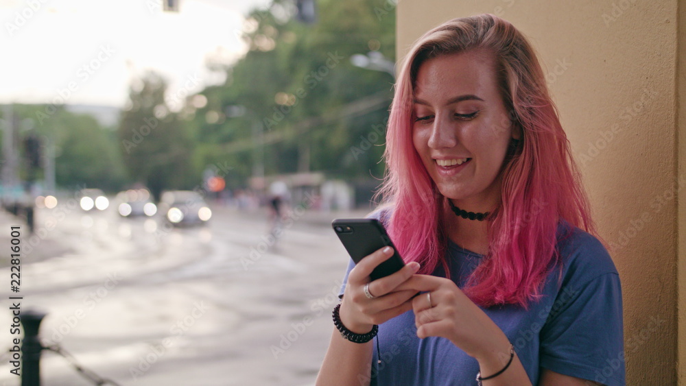 A young woman with a pink hair using a phone in the city street. Close-up shot. Soft focus