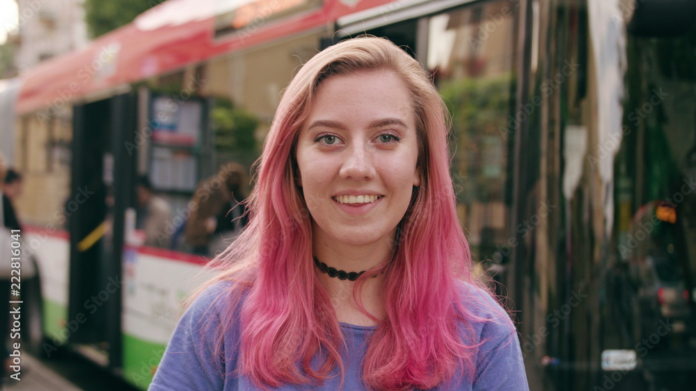 A happy smiling woman with a pink hair in the city street. Medium shot. Soft focus