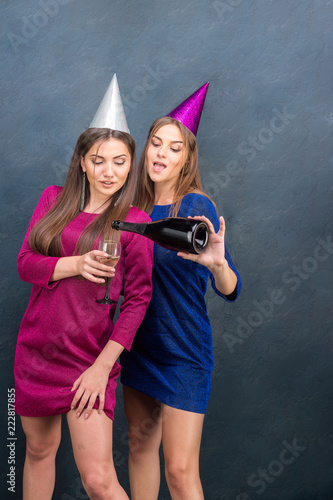 Beautiful girls in dresses celebrate a new year party enjoy champagne.Young women laughing, dansing, having fun and enjoy a holiday on a blue background.Concept of a holiday.New Year, birthday, party