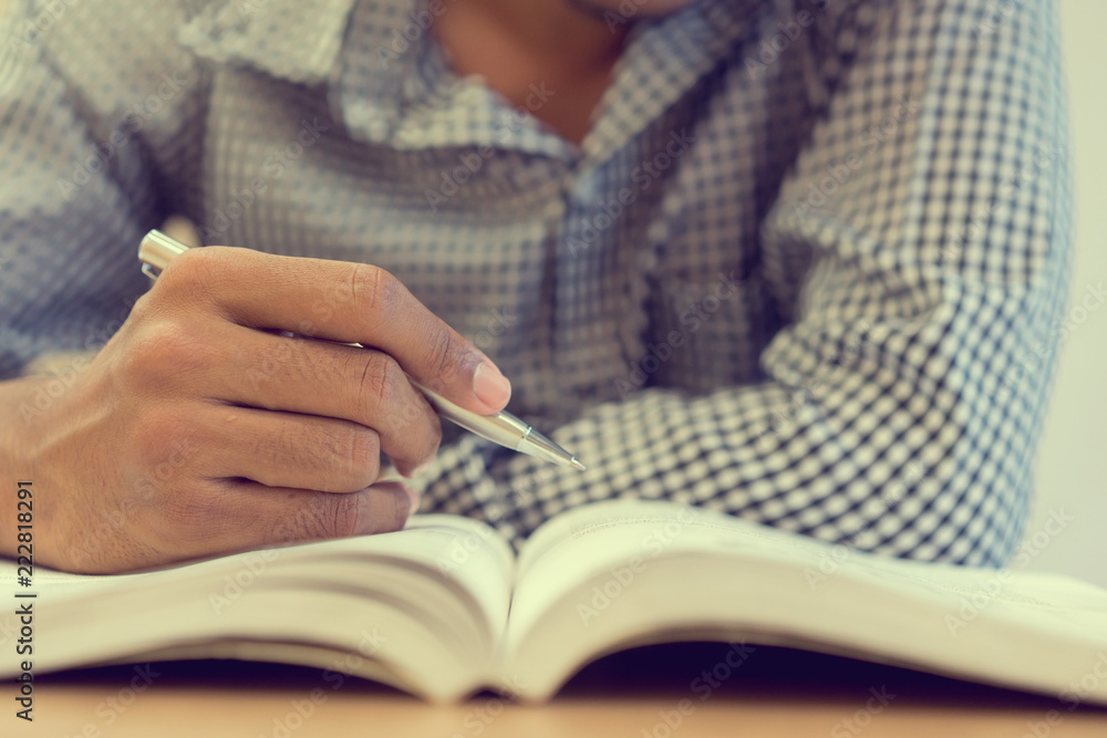 close up on student man hand using ballpoint pen and reading text book at library for examination in high school or university